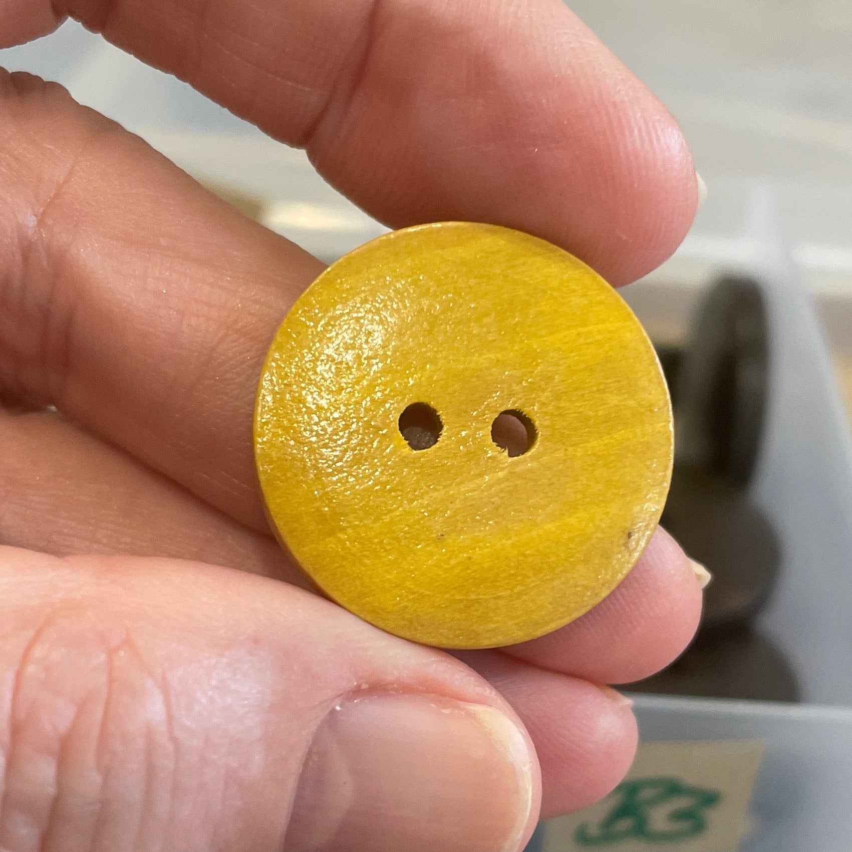 Hand holding a yellow button with a clear container of blue buttons in the background.