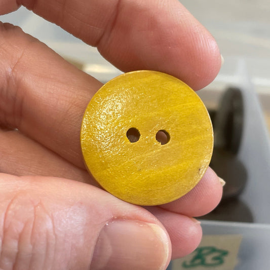 Hand holding a yellow button with a clear container of blue buttons in the background.