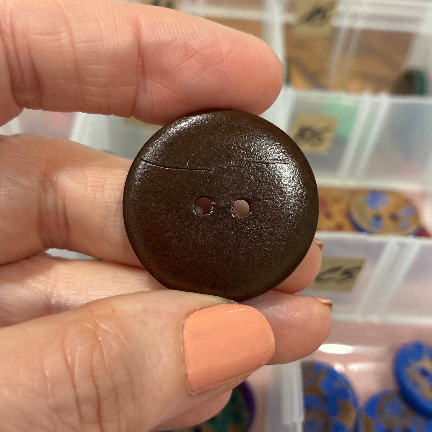 Brown button held by a hand with a container of buttons in the background
