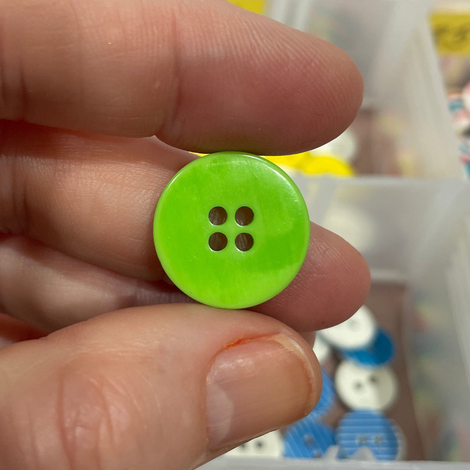 Green button held between fingers with a container of buttons in the background