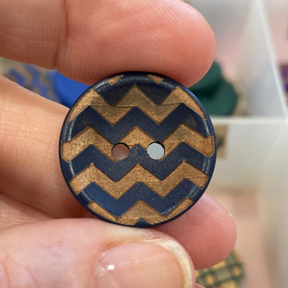 Hand holding a button with a zigzag pattern against a background of various buttons.