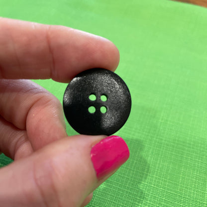 Black button held between fingers against a green background