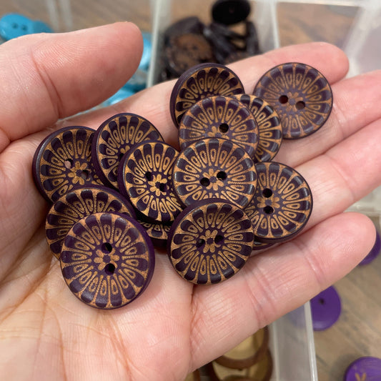 Hand holding decorative wooden buttons with a blurred background of more buttons.
