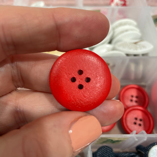 Red button held between fingers with blurred background of buttons and ribbons