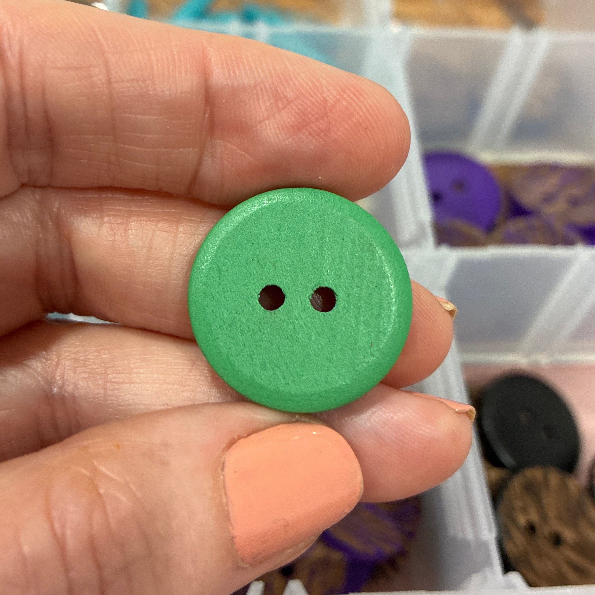 Green button held in a hand with a container of buttons in the background