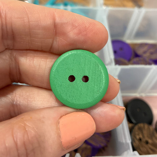 Green button held in a hand with a container of buttons in the background
