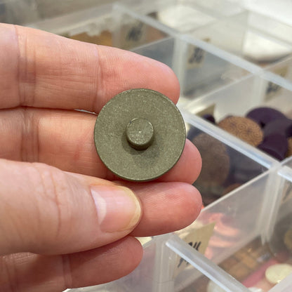 Hand holding a button in front of an open container with various items.