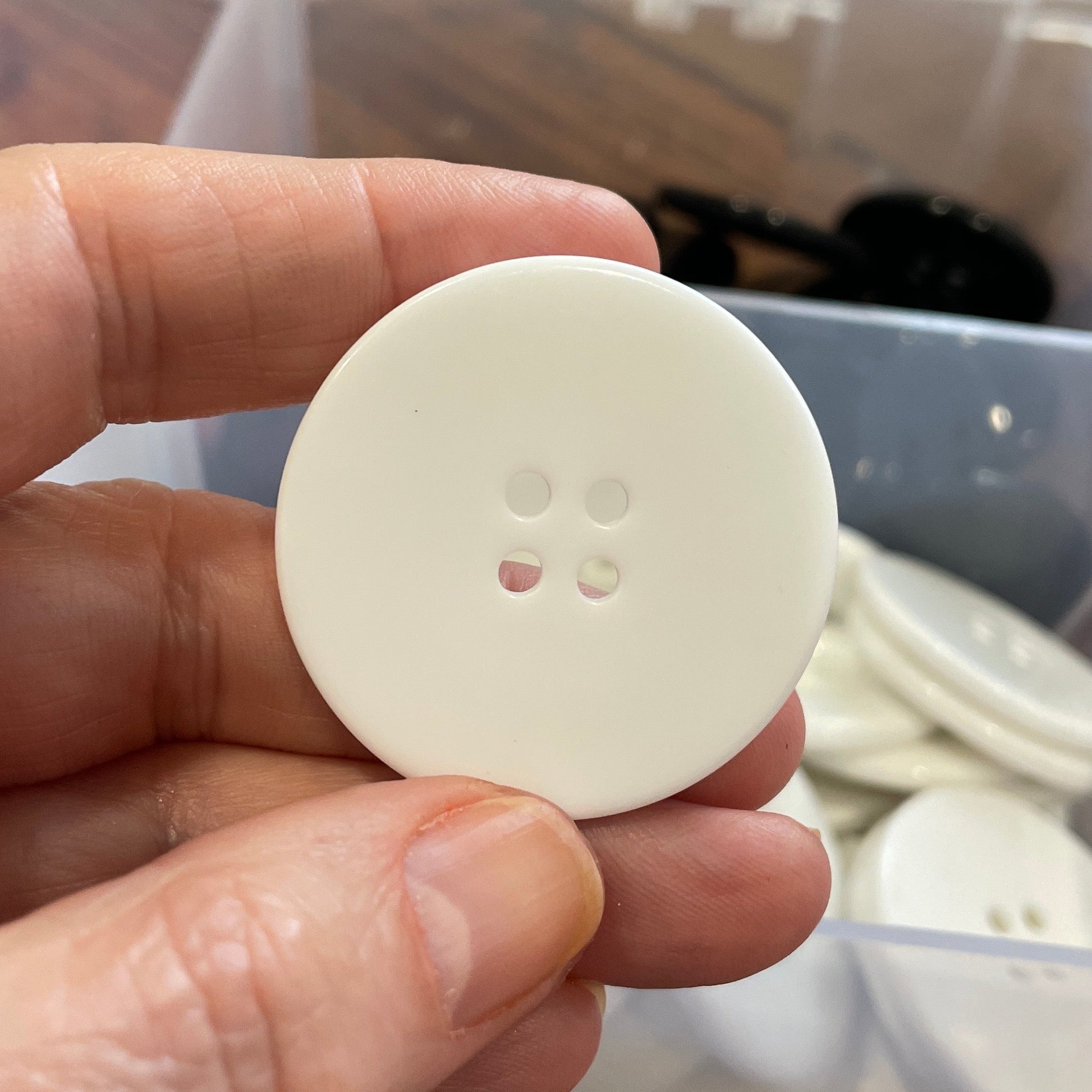 Hand holding a white button with  a container of buttons in the background.