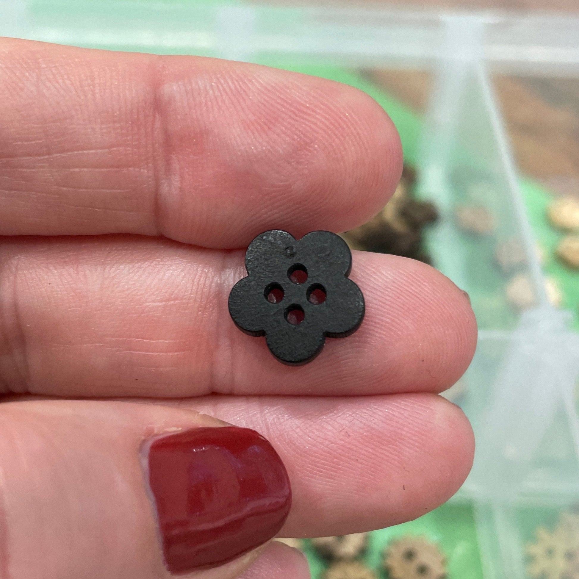 Hand holding a small black flower-shaped button with buttons in the background