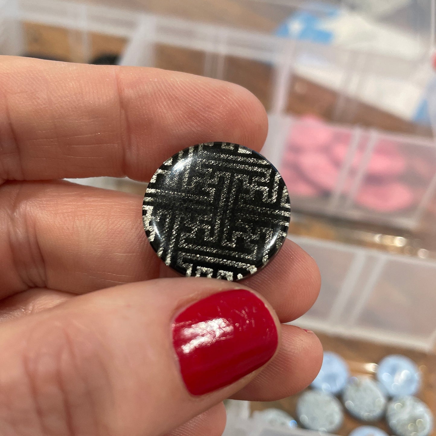 Hand holding a black and white patterned earring with a blurred background of jewelry boxes.