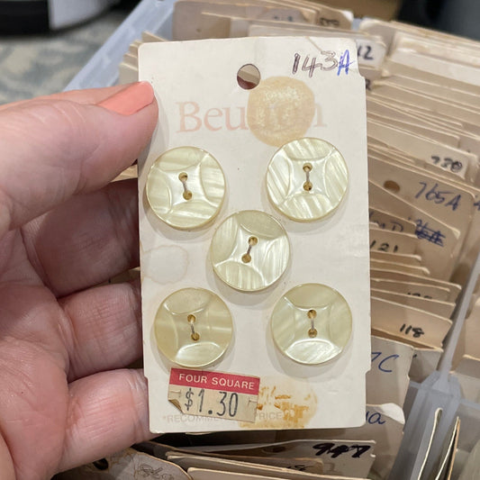 Hand holding a card with gold buttons in front of a container filled with similar cards.