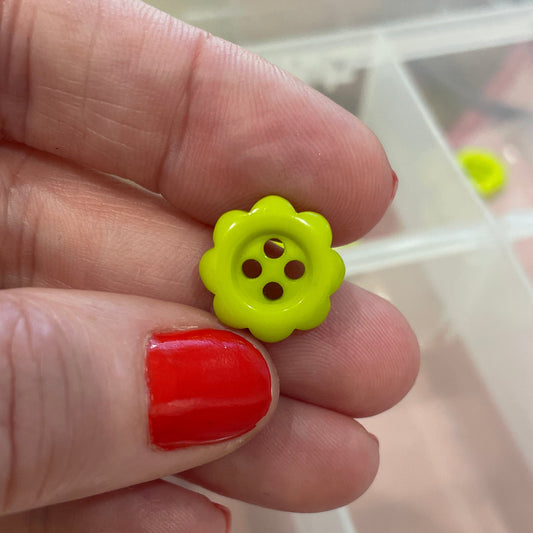 Hand holding a yellow flower-shaped button with a clear container of buttons in the background