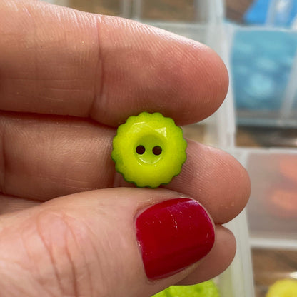 Hand holding two small green buttons with smiley faces against a background of button containers.
