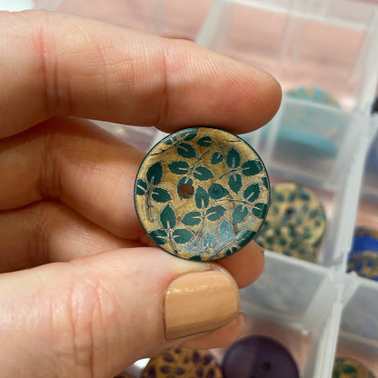 Hand holding a decorative button with a leopard print pattern over a container of similar buttons.