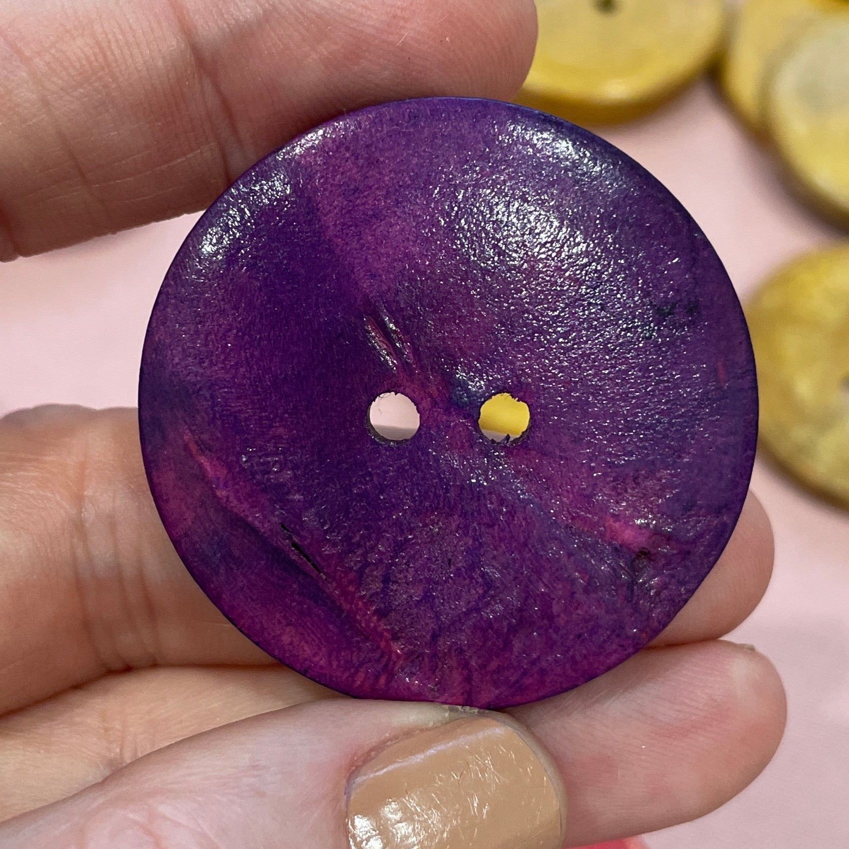 Hand holding a purple button with other colorful buttons in the background