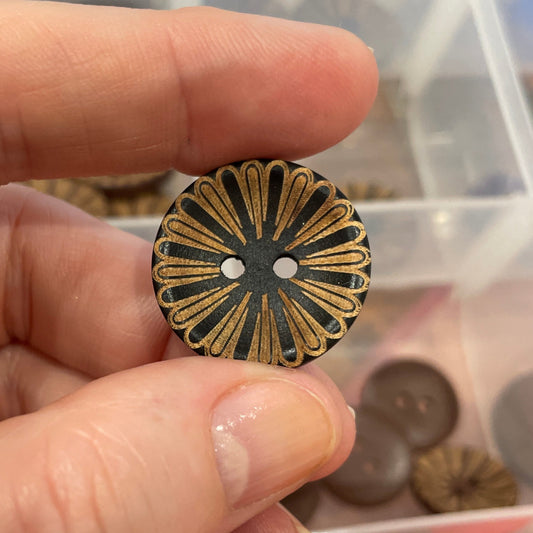 Hand holding a decorative button with a background of various buttons in a container.
