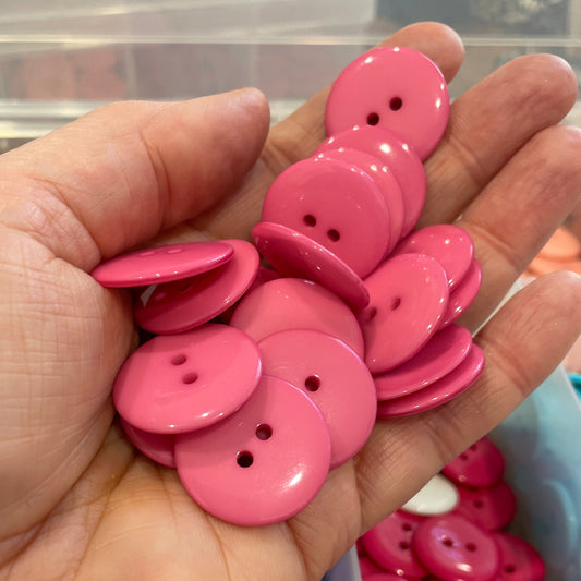 Hand holding pink buttons with a blurred background of more buttons.