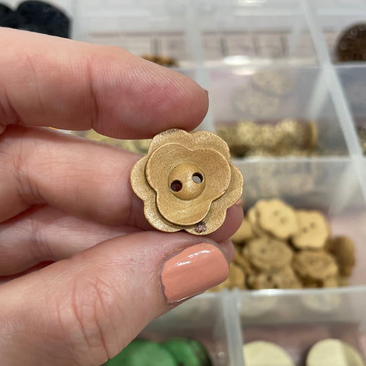 Hand holding a gold flower-shaped button with a container of buttons in the background