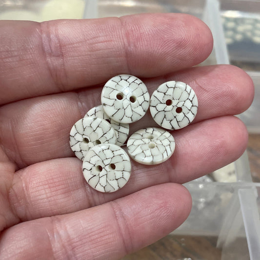 Three decorative buttons held in a hand with a clear plastic container in the background.