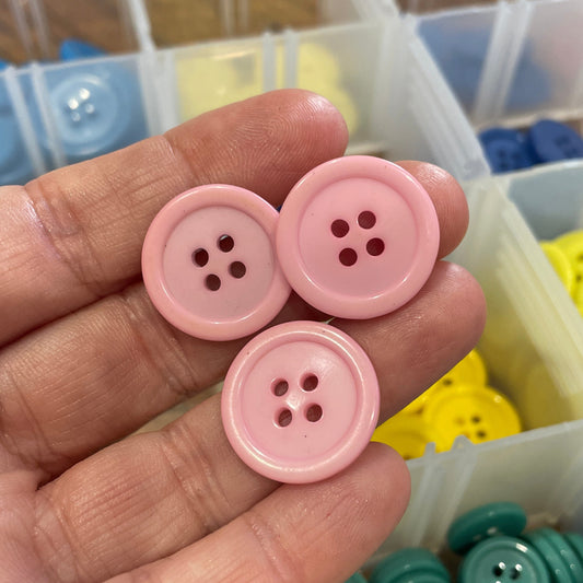 Hand holding pink buttons with a background of colorful buttons in containers