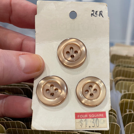 Three gold buttons on a card held by a hand with a blurred background