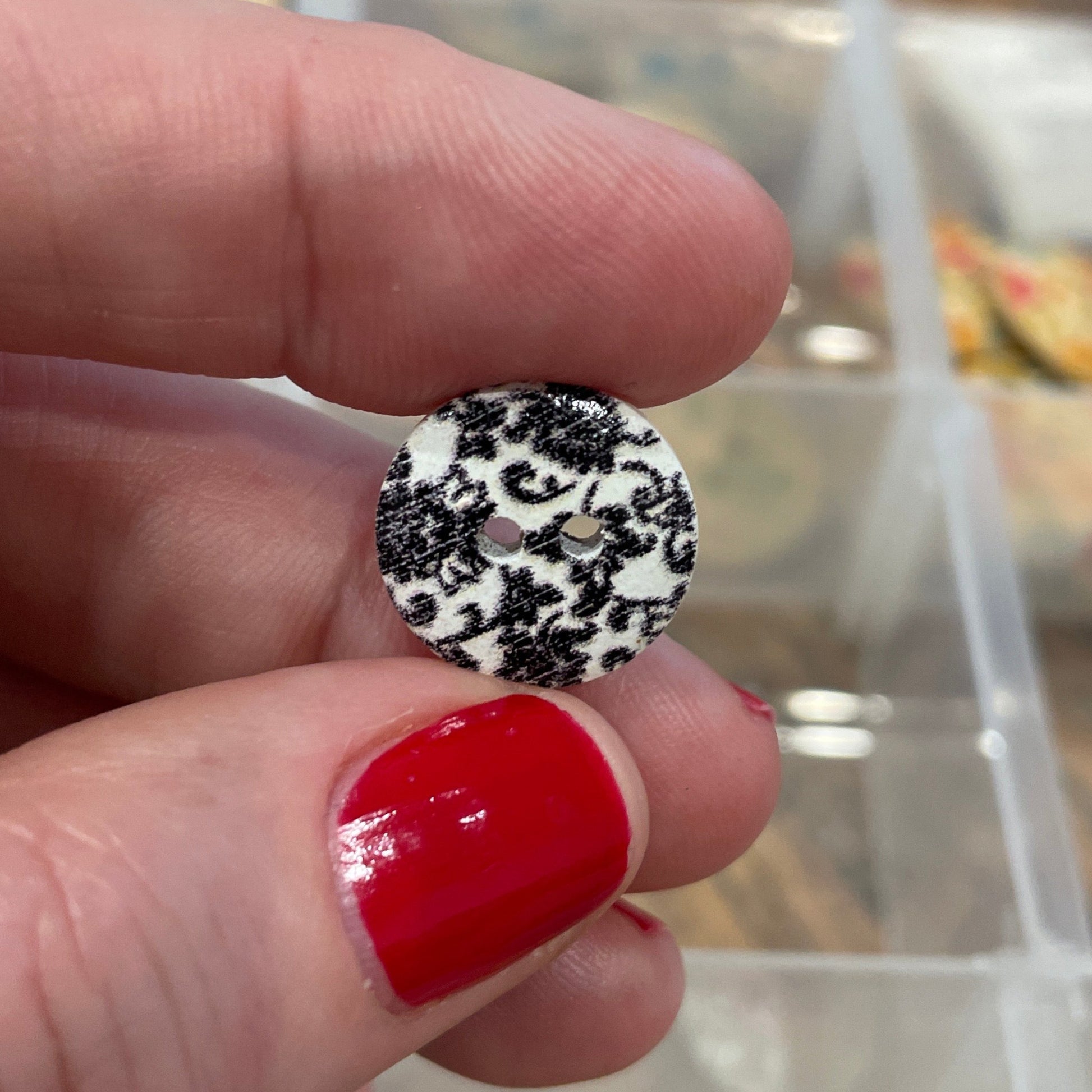 Hand holding a black and white polka dot button with a blurred background of a button collection.