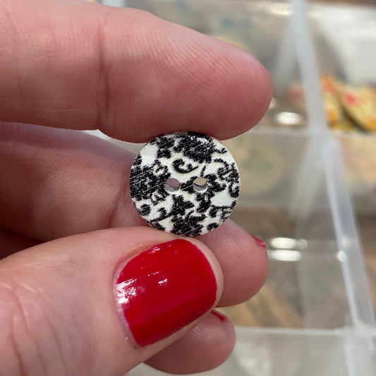 Hand holding a black and white polka dot button with a blurred background of a button collection.