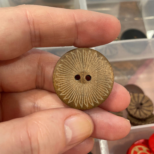 Hand holding a gold button with a clear container of various buttons in the background