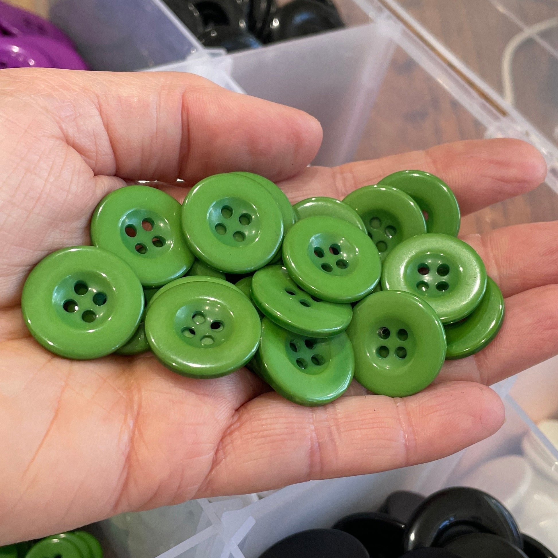 Hand holding green buttons with a container of buttons in the background
