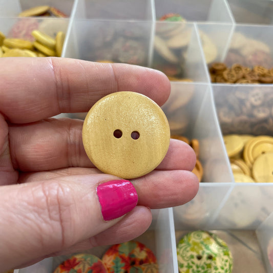 Hand holding a yellow button with two holes in front of a display case with various buttons.