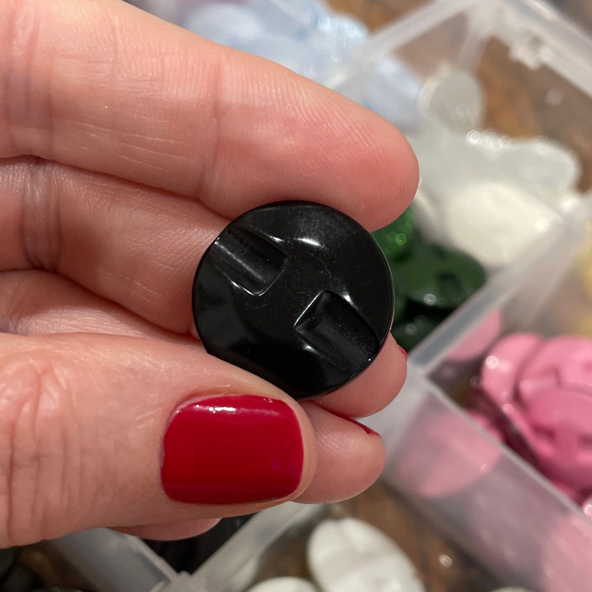 Hand holding a black button with a container of various buttons in the background