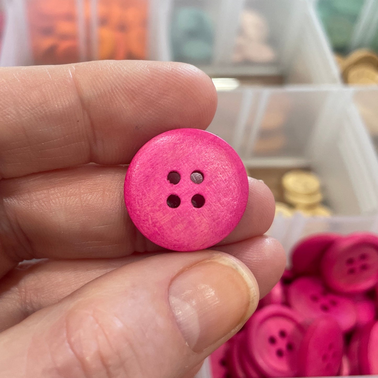 Pink button held between fingers with a container of buttons in the background