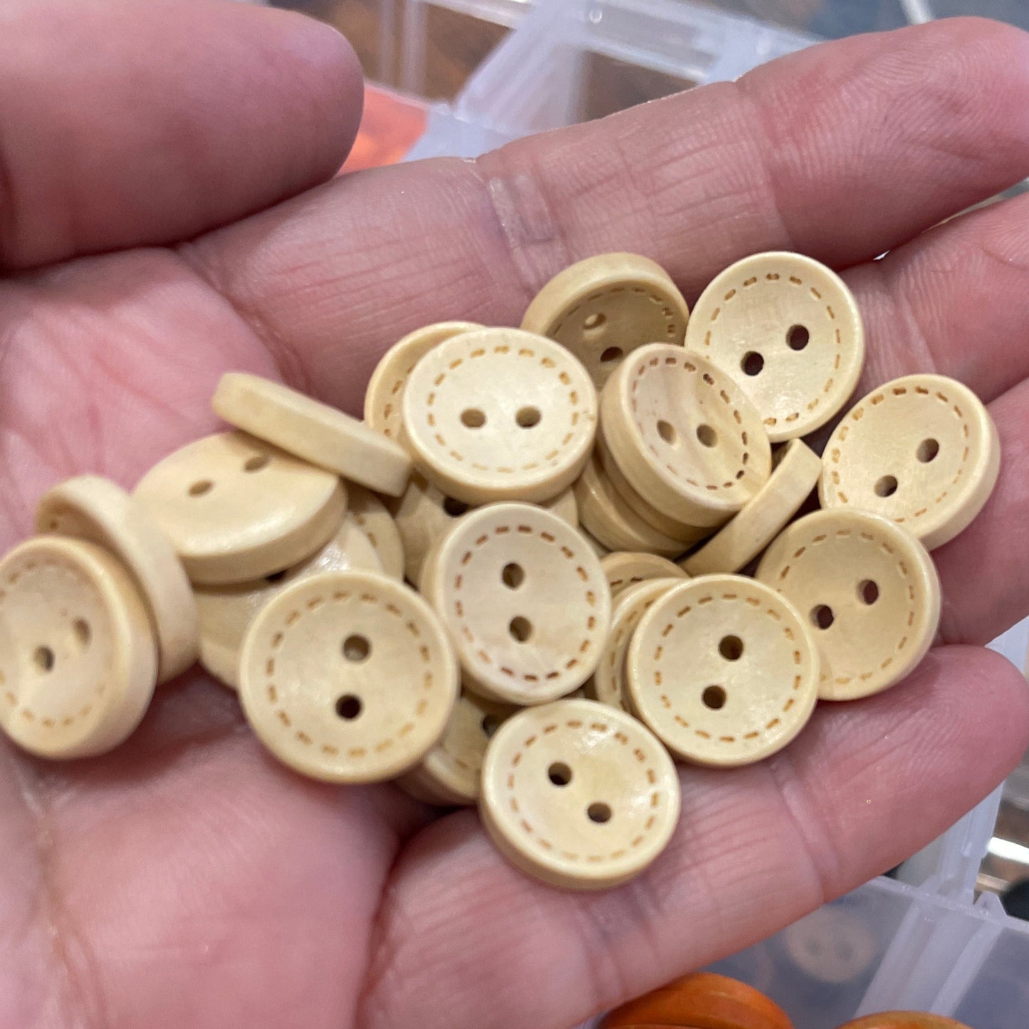 Hand holding beige buttons with a container of orange buttons on a wooden surface