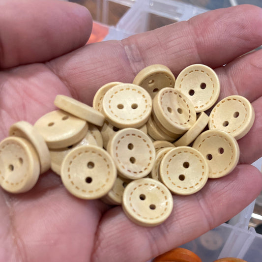 Hand holding beige buttons with a container of orange buttons on a wooden surface