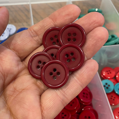 Hand holding red buttons with a container of assorted buttons in the background