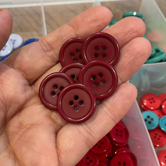 Hand holding red buttons with a container of assorted buttons in the background