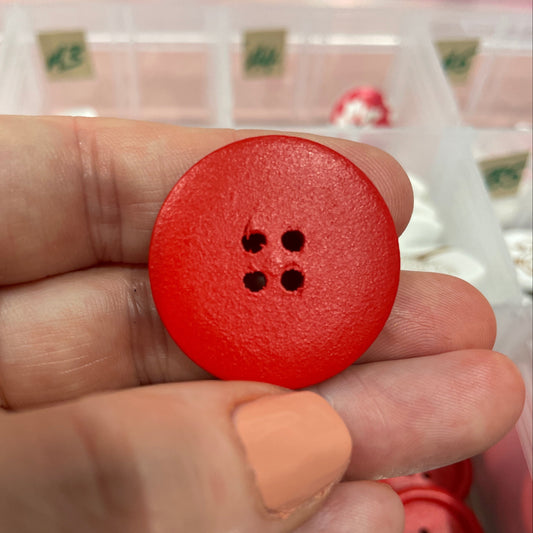 Red button held in a hand with a container of buttons in the background