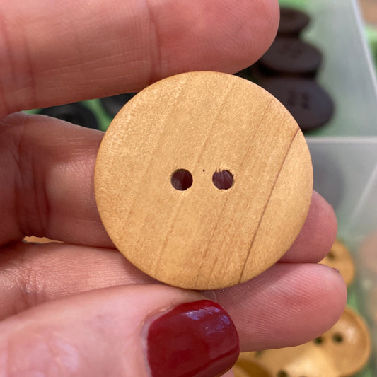 Hand holding a wooden button with a container of buttons in the background