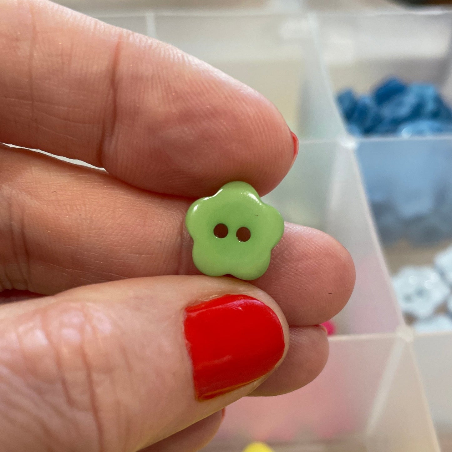 Hand holding a green button with a container of colorful buttons in the background