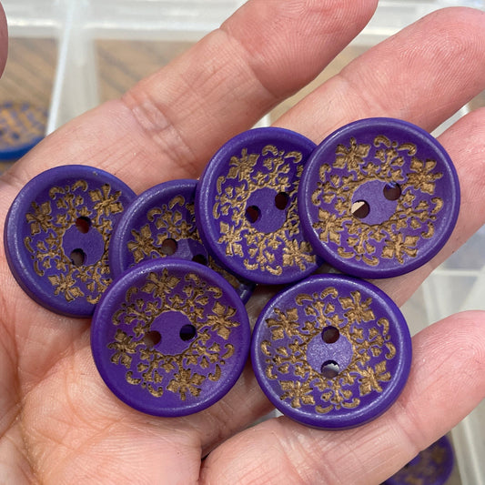 Hand holding purple buttons with floral patterns in front of a container filled with similar buttons.