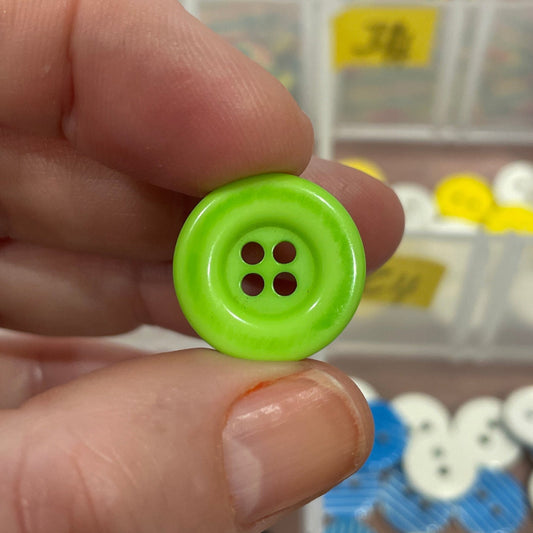 Hand holding a green button with a blurred background of button collection