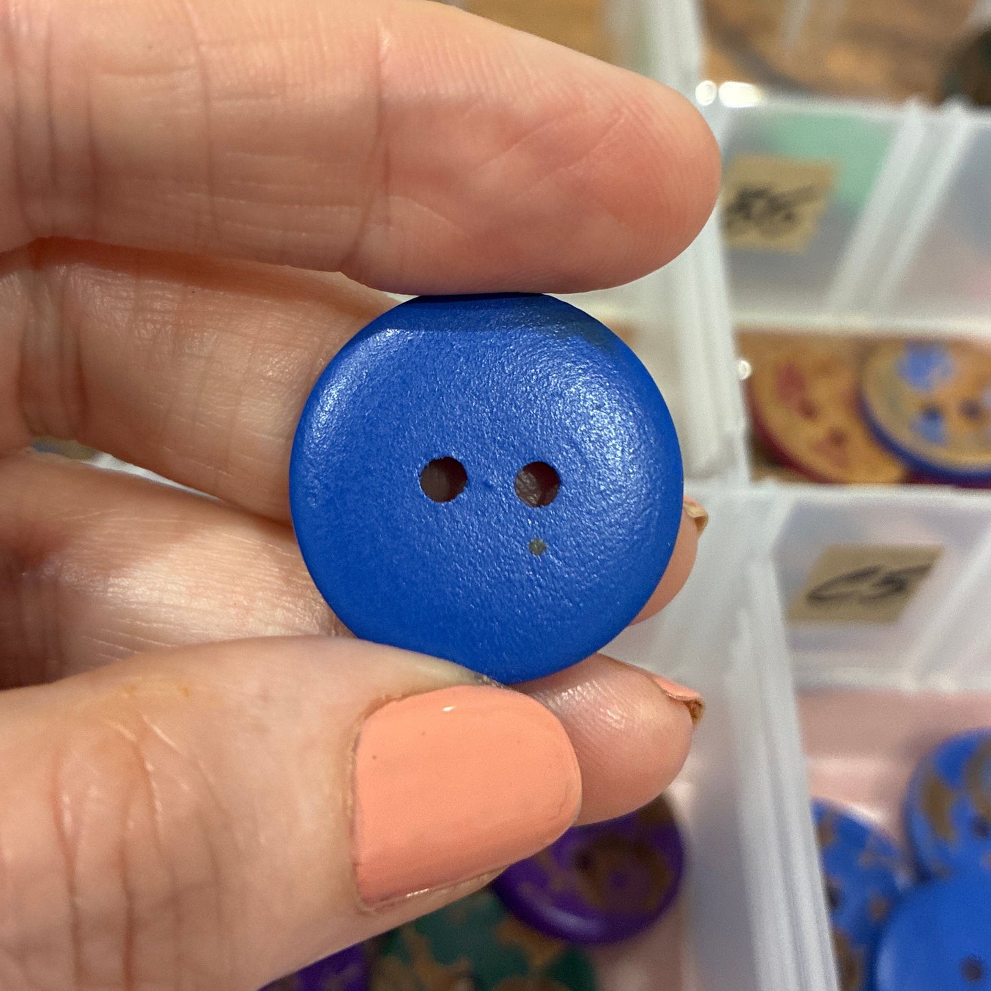 Hand holding a blue button with a container of buttons in the background