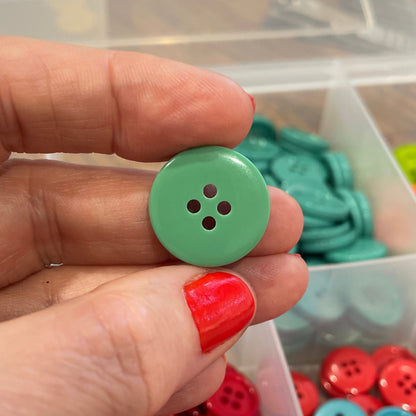 Hand holding a green button with a background of colorful buttons in containers.