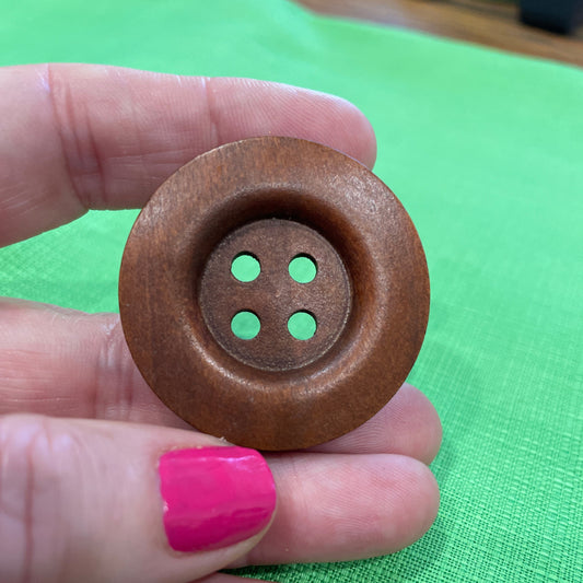 Wooden button held between fingers against a green background