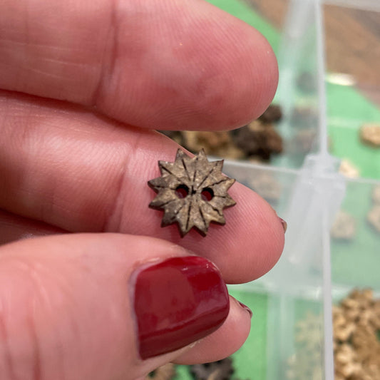 Hand holding a small decorative button  with a container of similar items in the background