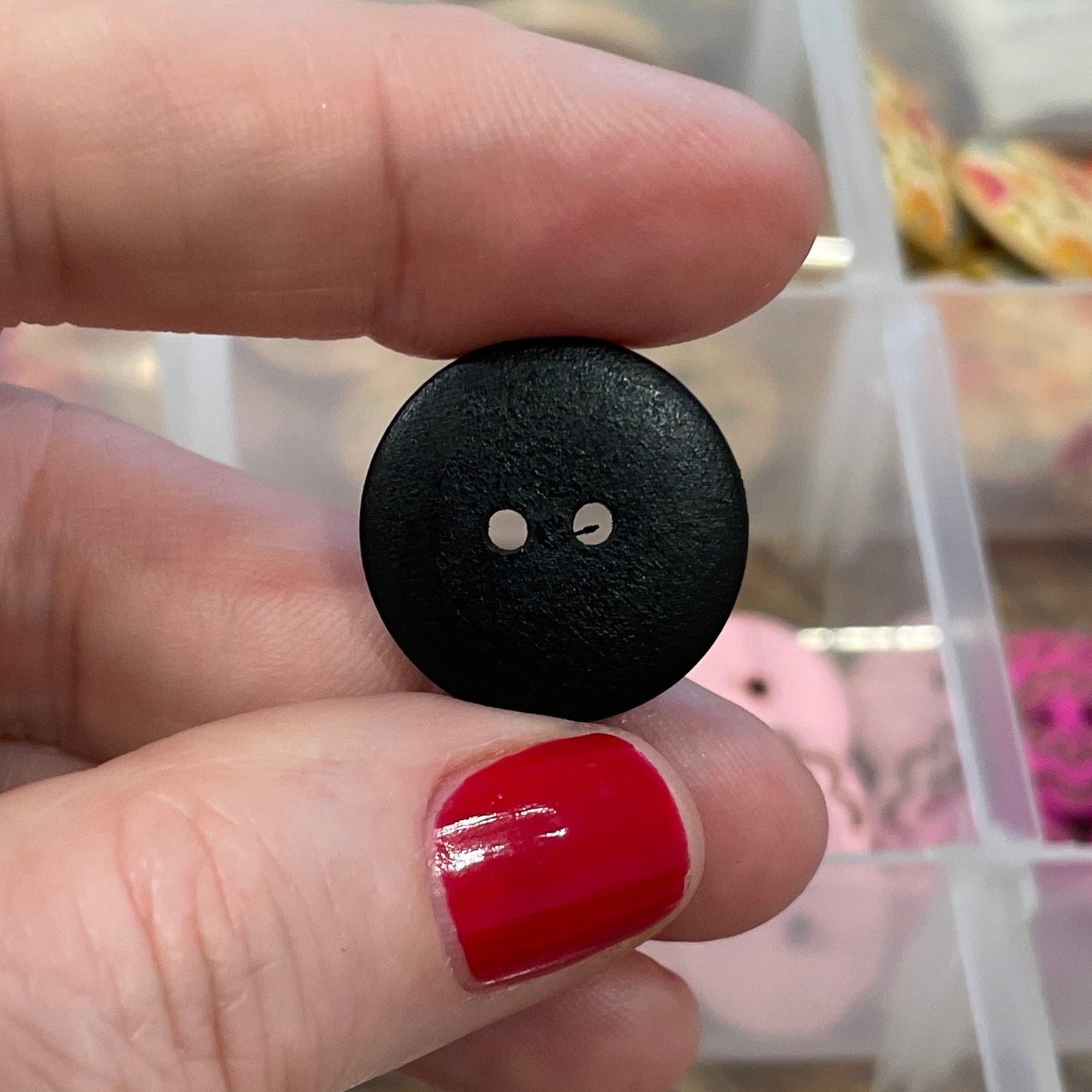 Hand holding a black button with a clear container of buttons in the background