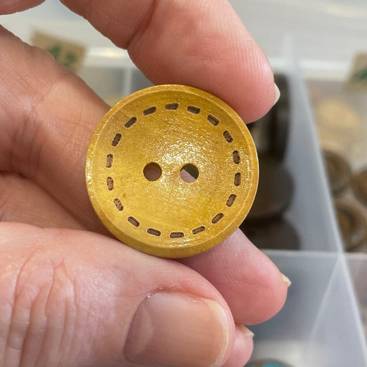 Hand holding a gold button with a container of blue buttons in the background