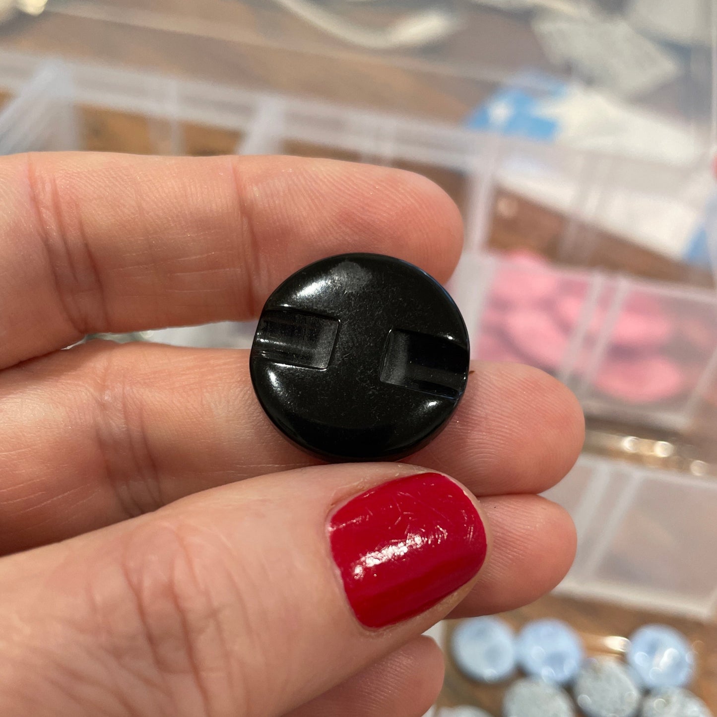 Hand holding a black button with a blurred background of assorted buttons in containers.