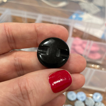 Hand holding a black button with a blurred background of assorted buttons in containers.