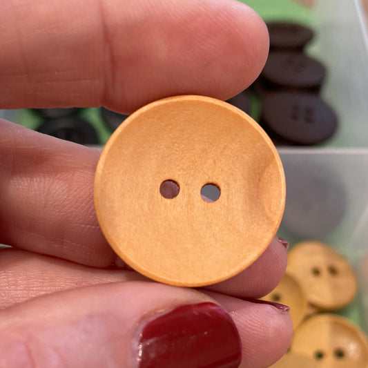 Hand holding a gold button with a container of buttons in the background